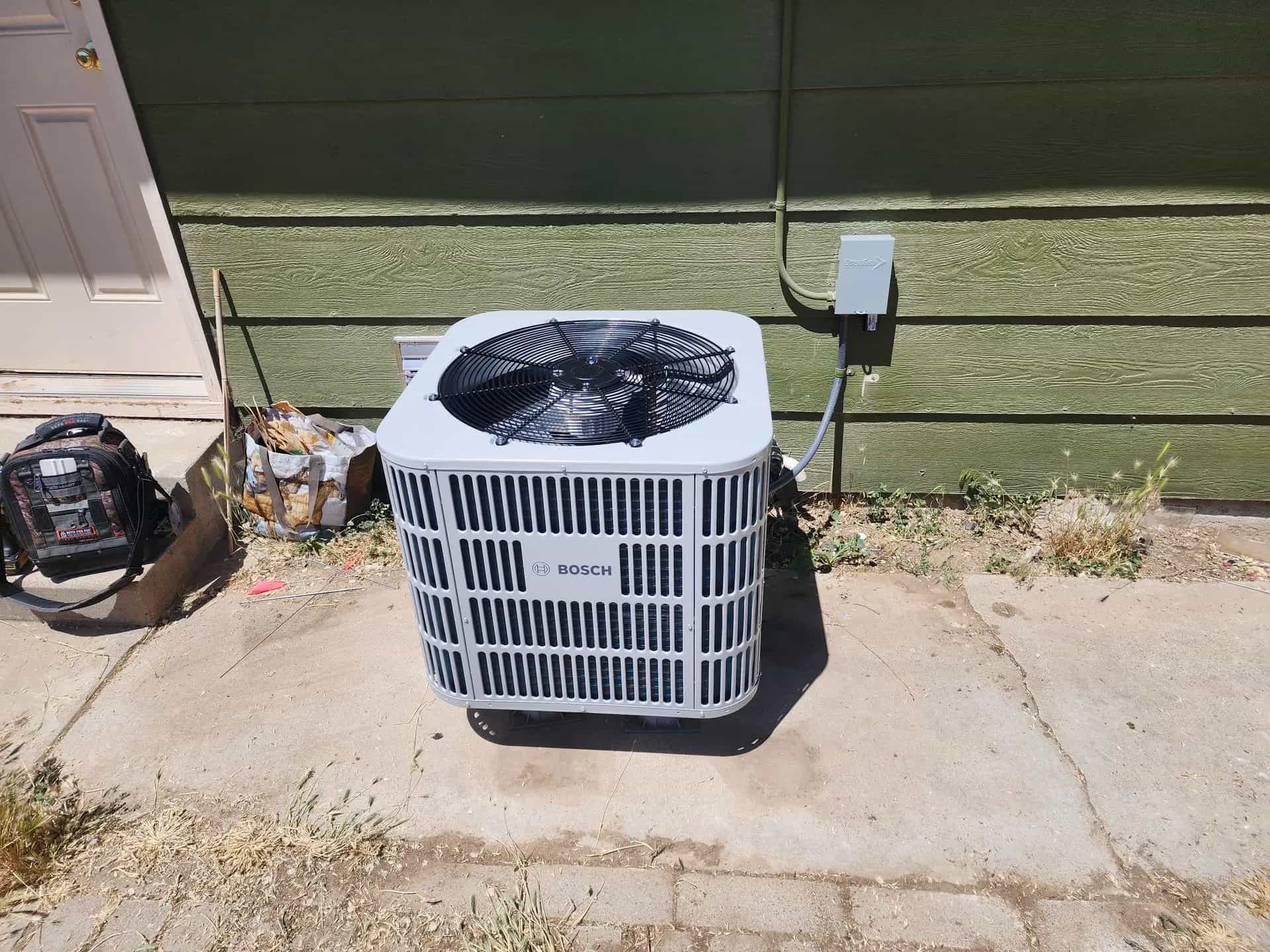 New Bosch heat pump condenser on a pad beside a house