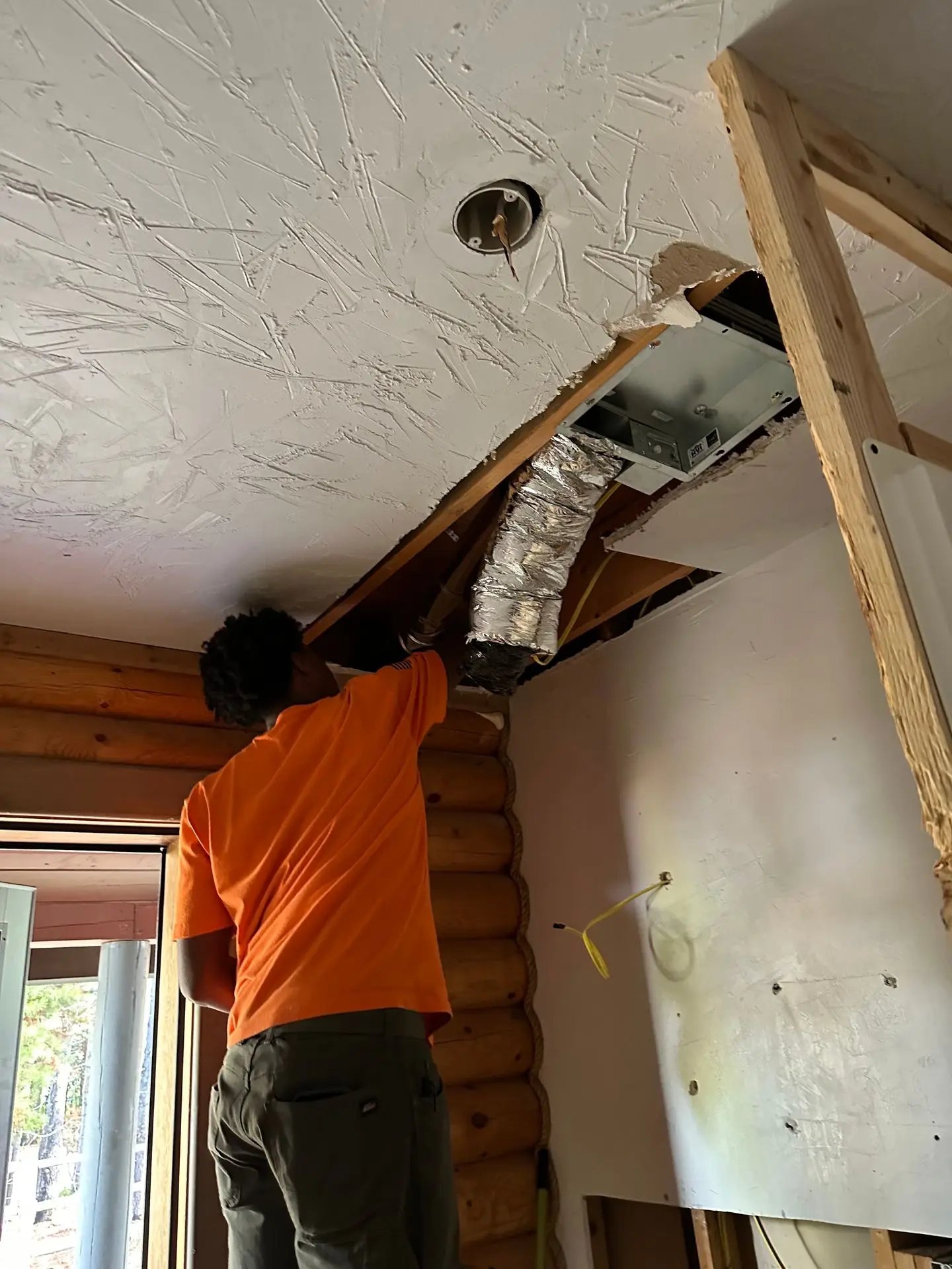 Technician fitting ductwork into a log home ceiling during a remodel